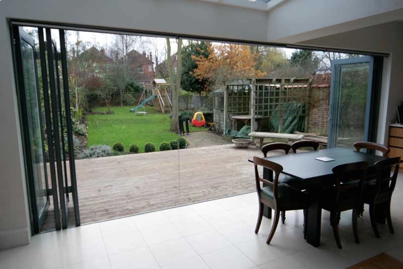 frameless glass aluminium bifold doors almost fully opened, looking onto a patio and garden