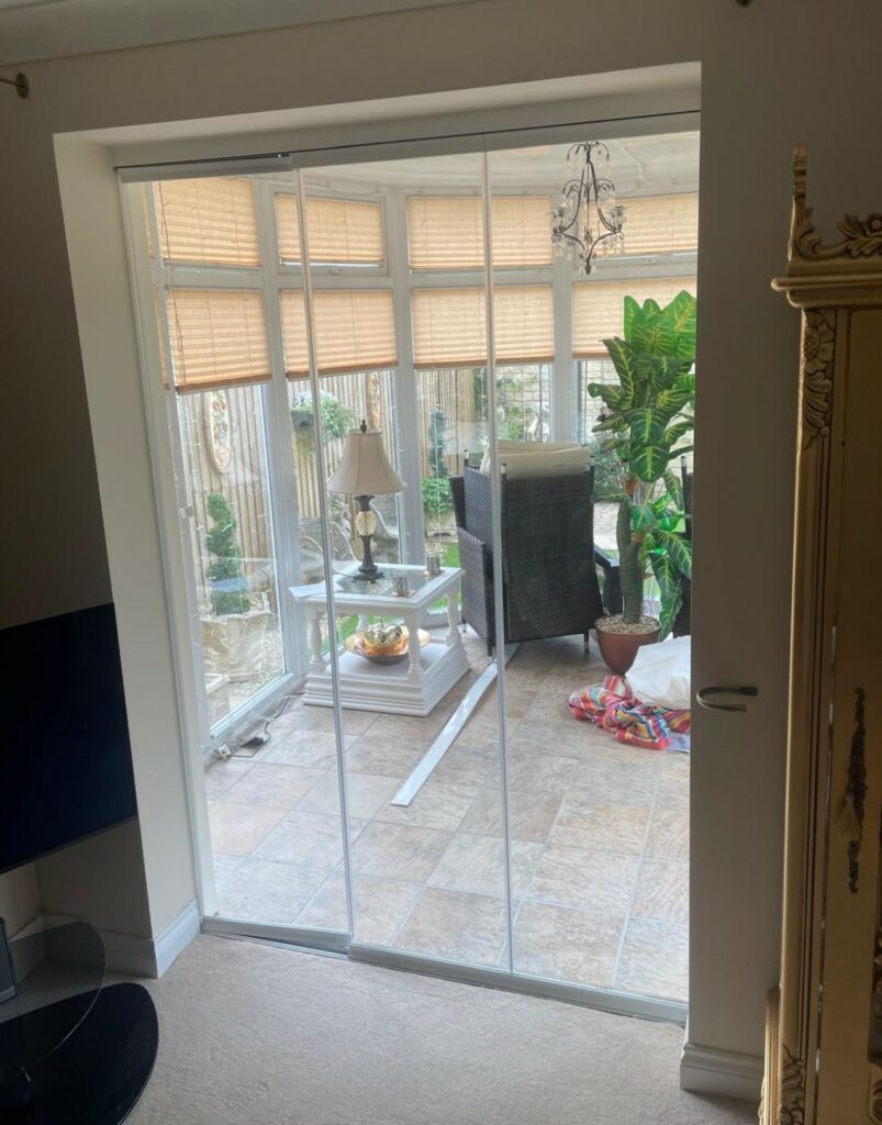 Frameless 3 panel glass panelled doors between a living room and a conservatory